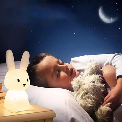 Un enfant endormi paisiblement, tenant son doudou dans ses bras sous la lumière de sa veilleuse bébé Glowbit™ en forme de lapin