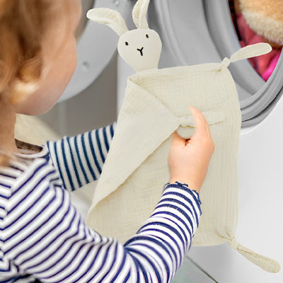 Enfant pli son doudou bébé devant la machine à laver