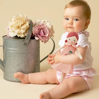 fillette assise par terre, sa poupée chiffon dans ses bras, à côté d'elle, il y a un arrosoir avec des fleurs