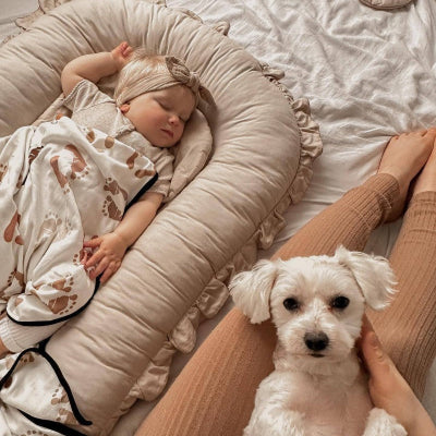 Une fillette endormie sur le côté dans son reducteur de lit HaveSaf™ couleur beige, et juste à côté d'elle, un chien posé sur les genoux de sa maîtresse. 