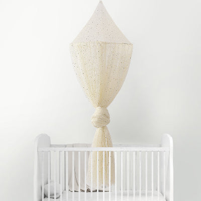 Une jolie moustiquaire pour lit bebe champagne scintillante délicatement nouée enveloppe de douceur le lit bébé blanc qu'elle surplombe.