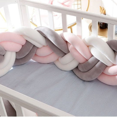 Un lit bébé blanc agrémenté d'une tresse tour de lit aux teintes pastel rose, blanc et gris créant une atmosphère chaleureuse et rassurante