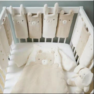 Un lit bébé blanc est entouré d'un tour de lit modulable compose de coussinets doux décorés d'oursons et de lapins créant un cocon chaleureux assorti au linge et au doudou.