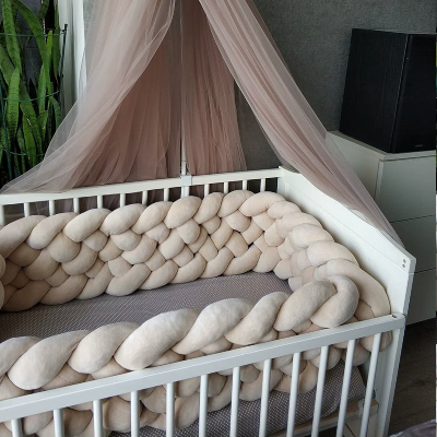 Un lit bébé blanc est joliment décoré d'un tour de lit tressé beige créant une atmosphère apaisante