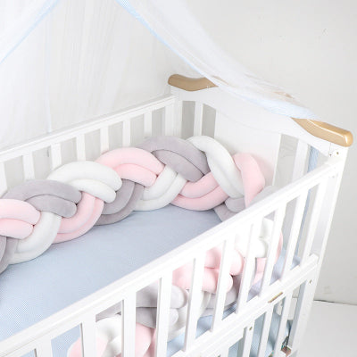 Un lit bébé blanc dans lequel est installée une tresse tour de lit aux couleurs douces rose pastel blanc et gris offrant une ambiance cocooning et sécurisante.