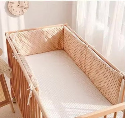 Le lit bébé en bois est entouré d'un tour de lit matelasse beige à texture gaufrée créant un espace doux, lumineux et confortable.
