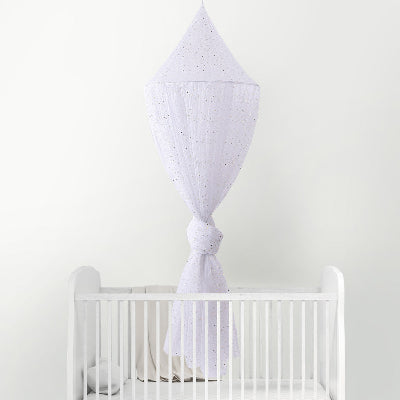 Une moustiquaire pour lit bebe blanche a pailleté suspendue et nouée en son centre surplombe un lit bébé blanc