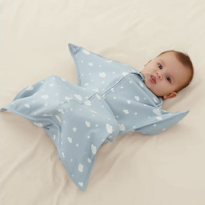 Un petit bébé allongé paisiblement sur un lit , enveloppé dans une turbulette gigoteuse bleu ornée de motifs en forme de nuages et d'étoiles