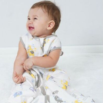 Un petit bébé assis tranquillement en souriant, bien au chaud dans une gigoteuse turbulette décorée de monstres rigolos