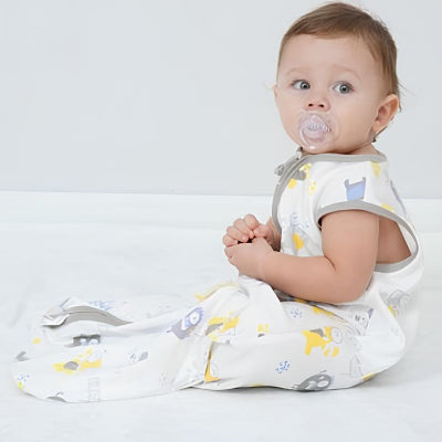 Un petit bébé est assis, bien au chaud dans une gigoteuse turbulette décorée de monstres rigolos.