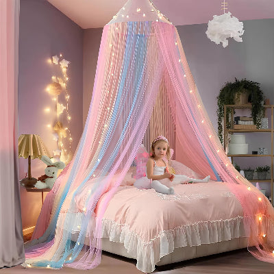 Une petite fille est assise calmement sur son lit, enveloppée par une moustiquaire pour lit suspendue aux couleurs pastel de l'arc-en-ciel qui flotte autour d'elle et donne à la chambre.