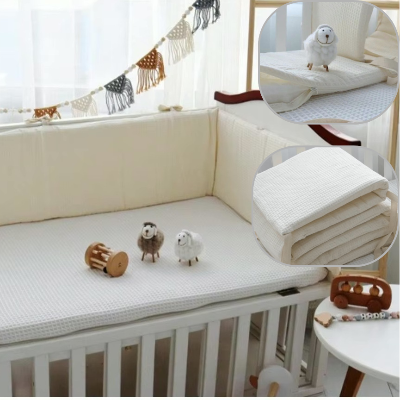 Un tour de lit bébé complet gaufré beige avec de petits jouets en bois dont deux moutons poses sur le lit