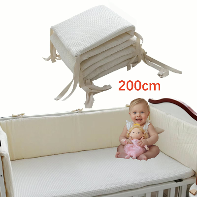 Un tour de lit bébé complet moelleux en tissu gaufré beige entoure le berceau offrant une protection douce tandis qu'un bébé souriant joue assis à l'intérieur.