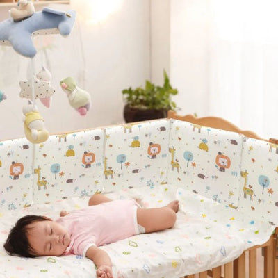 Le tour de lit bebe rembourré, décoré de petits animaux de la forêt, enveloppe le lit où bébé dort paisiblement dans une atmosphère tendre et apaisante.
