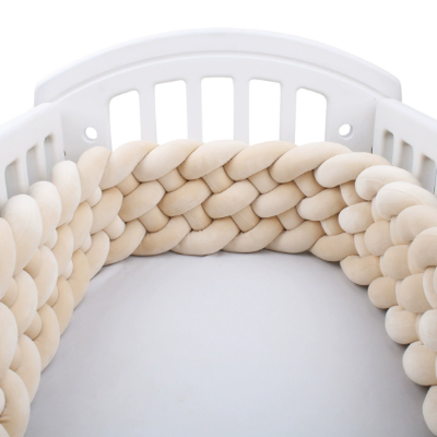Un tour de lit tressé épais de couleur beige entoure un lit bébé blanc qui apporte une touche délicate et raffinée