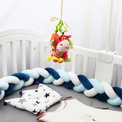 Un tour de lit tresse aux tons bleu, blanc et turquoise est installé tout autour d'un lit bébé blanc accompagne de vêtements assortis.