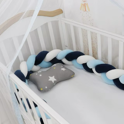 Un tour de lit tresse aux tons bleu, blanc et turquoise est installée tout autour d'un lit bébé blanc