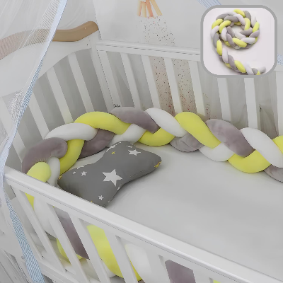 Une tresse de lit 4 m jaune, blanche et grise entoure l’intérieur d’un lit bébé blanc, accompagnée d’un coussin gris étoilé.
