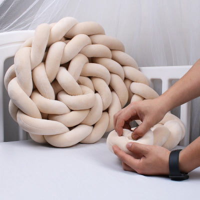 tresse de lit bebe beige moelleuse est soigneusement façonnée à la main posée sur un lit bébé blanc