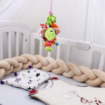 Une tresse de lit bebe beige repose délicatement sur un lit bébé blanc parfaitement assortie aux petits vêtements poses au centre