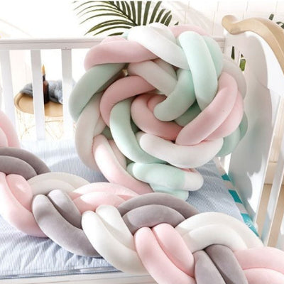 Une tresse tour de lit aux couleurs pastel est installée dans un lit blanc avec une partie enroulée en boule décorative créant une ambiance douce et confortable.