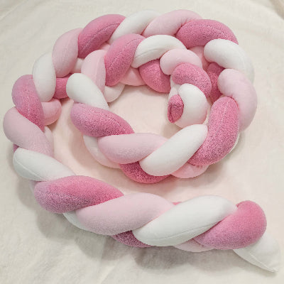 Une tresse tour de lit aux douces teintes rose et blanc déposée sur le lit de bébé
