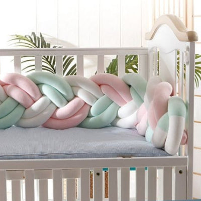 Une tresse tour de lit rose pastel blanche et vert menthe installée dans un lit bébé blanc diffuse une ambiance douce et apaisante.